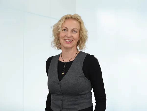 Auf dem Bild ist eine blonde Frau in einem schwarzen Shirt und grauer Weste zu sehen. Sie lächelt freundlich in die Kamera.