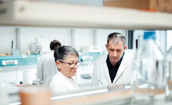 Auf dem Bild sind ein Labormitarbeiter und eine Labormitarbeiterin in weißen Kitteln zu sehen.