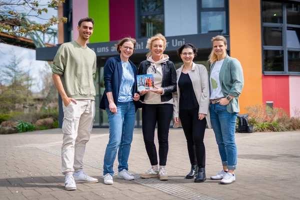 Fünf Personen posieren lächelnd vor einem bunten Gebäude.