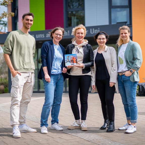 Fünf Personen stehen lächelnd vor einem bunten Gebäude.