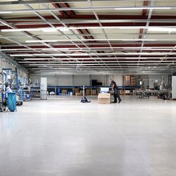 Auf dem Bild ist eine große Industriehalle zu sehen, rechts und links stehen Maschinen und Gerätschaften. 