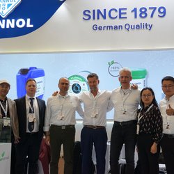 Auf dem Bild ist eine Gruppe von sieben Personen vor dem Messestand von Stannol zu sehen. Sie tragen förmliche Kleidung, haben sich die Arme um die Schultern gelegt und lächeln freundlich in die Kamera.