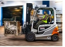 Mann fährt Gabelstapler mit Metallkiste in Lagerhalle.