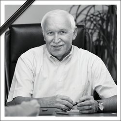 Auf dem schwarz-weiß-Bild ist ein älterer Herr mit weißen Haaren und weißem Hemd an einem Schreibtisch zu sehen. Er lächelt freundlich in die Kamera. Das Foto trägt ein Trauerband.