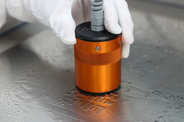 Ein orangefarbener Ultraschallschwingkopf wird per Hand über eine mit Lotpaste verschmutzte Schablone geführt.