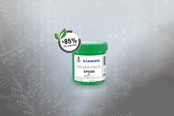 The picture shows a green tin of Stannol solder paste SP6000. It bears a white label with the Stannol logo and other product specifications. The background consists of a colour gradient of different shades of grey. Next to the can is a button with the text 85 per cent CO2 reduction.