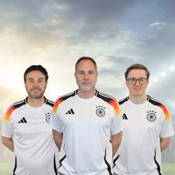 Auf dem Bild sind Iljan Sandtstedt, Thomas Kolossa und Nicolas Wiacker in Deutschland-Fußballtrikots zu sehen. Sie haben die Arme hinter dem Rücken verschränkt und lächeln freundlich in die Kamera.