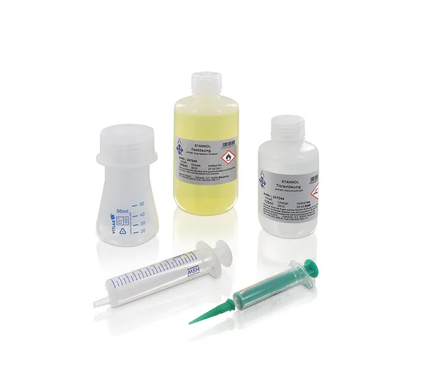 Auf dem Bild ist das Mini-Titrierset von Stannol zu sehen: Zwei kleine Fläschchen mit einer gelblichen und einer klaren Flüssigkeit, einem kleinen Kunststoff-Behälter sowie zwei verschiedene Spritzen.