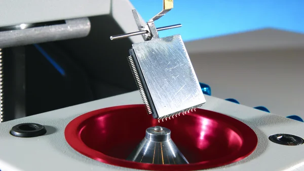 Auf dem Bild ist eine Benetzungswaage zu sehen. Ein Halter mit einem Bauteil wird langsam auf eine Lotkugel abgesenkt.