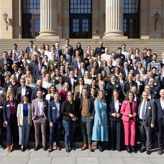 Auf dem Bild ist eine große Gruppe von Menschen auf einer Treppe vor den Säulen eines großen Gebäudes zu sehen.