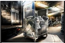 Metallkäfig voller Elektronikschrott in einem beleuchteten Lagerraum.