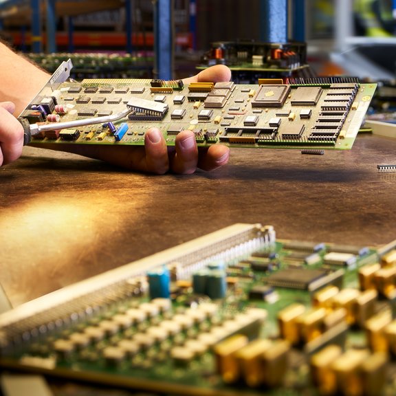 The picture shows a man in a blue T-shirt dismantling a circuit board. 