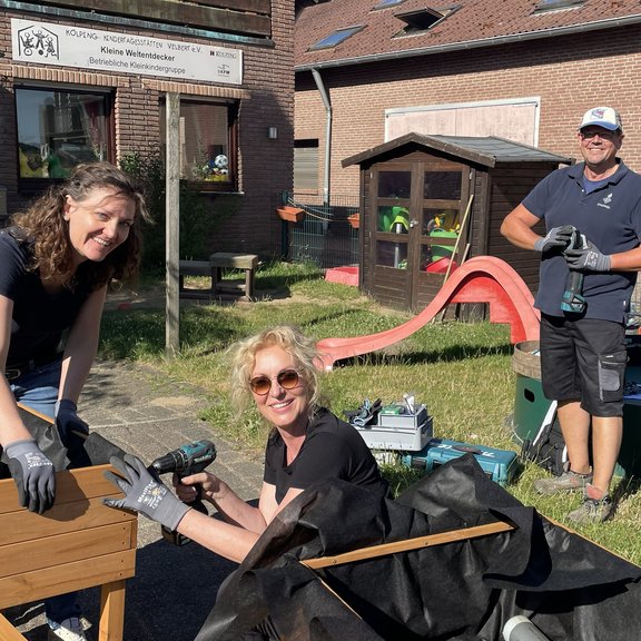 Drei Personen bauen im Freien einen Hochbeetkasten zusammen.