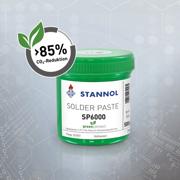 The image shows a green plastic container of solder paste from the brand Stannol. The label reads “Solder Paste SP6000” along with the “green connect” logo, symbolized by a green leaf. To the left above the container, there is a circular icon with a leaf and the text “85% CO₂ reduction.” The background is gray with schematic lines and dots, creating a technical, modern look. The image highlights Stannol’s sustainability efforts, specifically the 85% CO₂ reduction for this product.