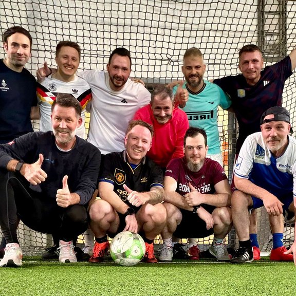 [Translate to Englisch:] Gruppe von Männern posiert auf einem Fußballplatz in sportlicher Kleidung.