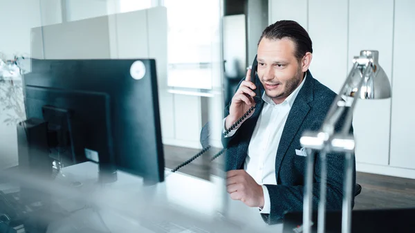 Mann im Büro telefoniert am Schreibtisch vor einem Computer.