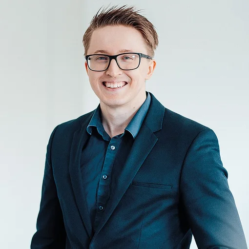 Auf dem Bild ist ein blonder junger Mann in blauem Hemd und Sakko zu sehen. Er trägt eine Brille und lächelt freundlich in die Kamera.