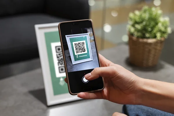 Auf dem Bild ist eine Hand zu sehen, die ein Smartphone hält, das einen QR-Code abscannt.