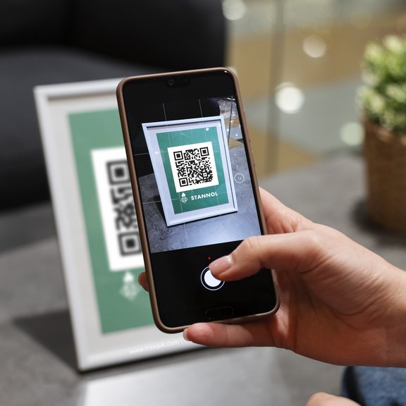 Auf dem Bild ist eine Hand zu sehen, die ein Smartphone hält, das einen QR-Code scannt.