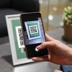 Auf dem Bild ist eine Hand zu sehen, die ein Smartphone hält, das einen QR-Code scannt.