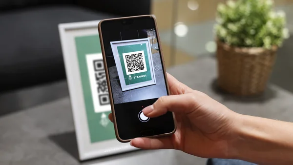 Auf dem Bild ist eine Hand zu sehen, die ein Smartphone hält, das einen QR-Code abscannt. 