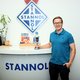 The picture shows a young blonde man with glasses at a Stannol counter. He is wearing a turquoise polo shirt, dark trousers and is holding a trophy in his hand.