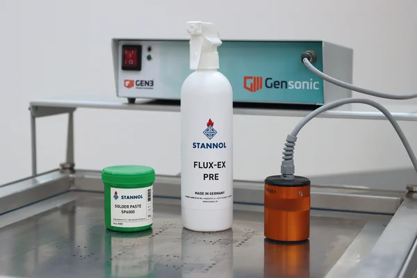 Auf dem Bild sind das Ultraschall-Reinigungsgerät Gensonic von Gen3 inklusive orangefarbenem Ultraschallschwingkopf, eine grüne Lotpastendose mit SP6000 Lotpaste von Stannol und eine weiße Sprühflasche Flux-Ex Pre-Reiniger von Stannol zu sehen.