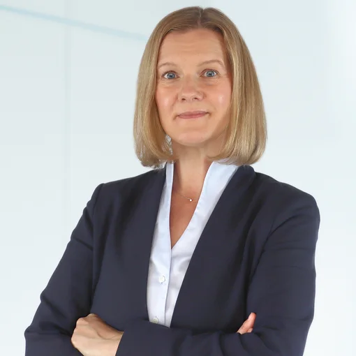 Auf dem Bild ist eine Frau mit halblange, blonden Haaren zu sehen. Sie trägt eine hellblaue Bluse und einen blauen Blazer. Sie lächelt freundlich in die Kamera.