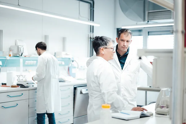 Auf dem Bild sind zwei Labormitarbeiter und eine Labormitarbeiterin in weißen Kitteln zu sehen.