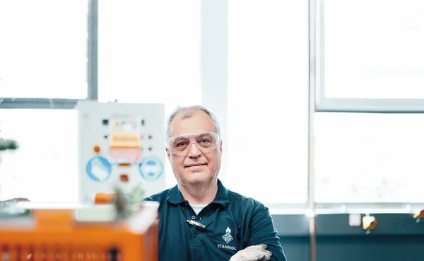 Auf dem Bild ist ein Mitarbeiter aus der Produktion zu sehen. Er trägt ein blaues Shirt, Arbeitshandschuhe und eine Schutzbrille. Er lächelt freundlich in die Kamera.