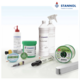 The picture shows various items from the Stannol range, such as a green solder paste tin, a spool of solder wire, a solder bar, a spray bottle of cleaning agent, desoldering braids and flux pens.