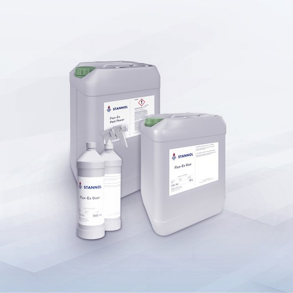 The picture shows three large canisters and two bottles of Flux-Ex cleaning agent from the Stannol brand. The canisters are grey and have green caps, with product names such as ‘Flux-Ex Post Power’ and ‘Flux-Ex Glue’ on the labels. In front of the canisters are two white bottles, one of which has a spray nozzle, also with the Stannol logo and labelling. The products are professional cleaning agents for the soldering industry.