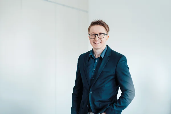 Auf dem Bild ist ein junger blonder Mann mit Brille zu sehen. Er trägt einen dunkelblauen Anzug und ein blaues Hemd. Er lächelt freundlich in die Kamera.