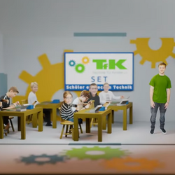 Das Bild zeigt einen Ausschnitt aus dem Weihnachtsvideo des Vereins Technik für Kinder. Kinder sitzen an verschiedenen Tischen und beschäftigen sich verschiedenen Aufgaben , zum Beipisel Löten Im Hintergrund ist eine Tafel mit dem Logo des TFK zu sehen.