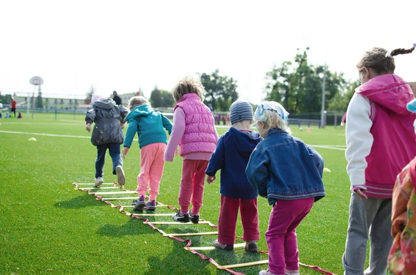 The image is a stock photo. It shows a row of children from behind playing a game of hopscotch.