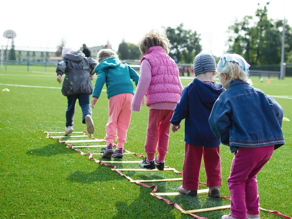 Bei dem Bild handelt es sich um ein Stock-Foto. Darauf sind eine Reihe Kinder von hinten zu sehen, die ein Hüpf-Spiel spielen.
