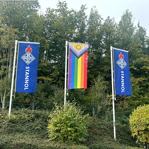 The picture shows three flags, two blue Stannol flags with logo on the right and left and a rainbow flag in the centre.