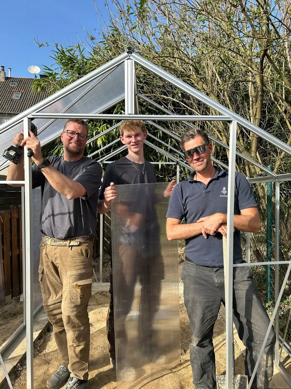 Drei Handwerker bauen ein Gewächshaus.