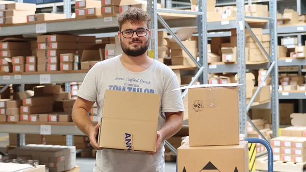 Mann mit Kartons in einem Lager mit Regalen voller Pakete.