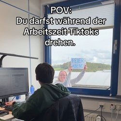 Auf dem Bild ist ein junger Mann am Arbeitsplatz vor seinem Rechner zu sehen. Am Fenster rechts von ihm geht eine junge Kollegin vorbei. Sie hält ein Schild hoch mit dem Schriftzug: Feierabend. Über das Bild ist der Schriftzug: POV Du darfst während der Arbeitszeit TikToks drehen gelegt.