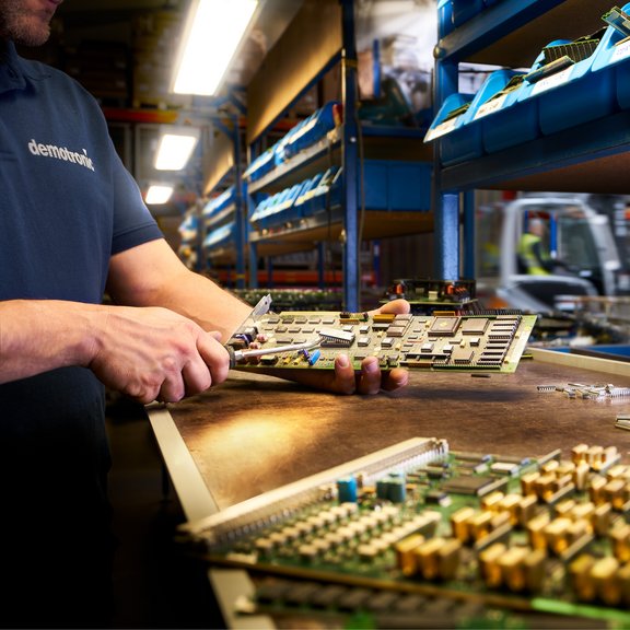 The picture shows a man in a dark blue T-shirt dismantling a circuit board.