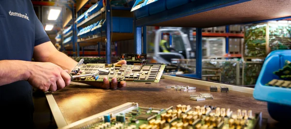 Mann arbeitet mit Leiterplatten in einer Werkstatt mit Regalen im Hintergrund.