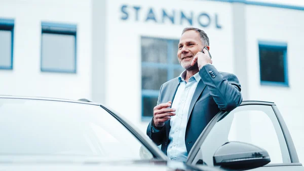 Mann telefoniert neben Auto vor Gebäude mit "STANNOL"-Schriftzug.