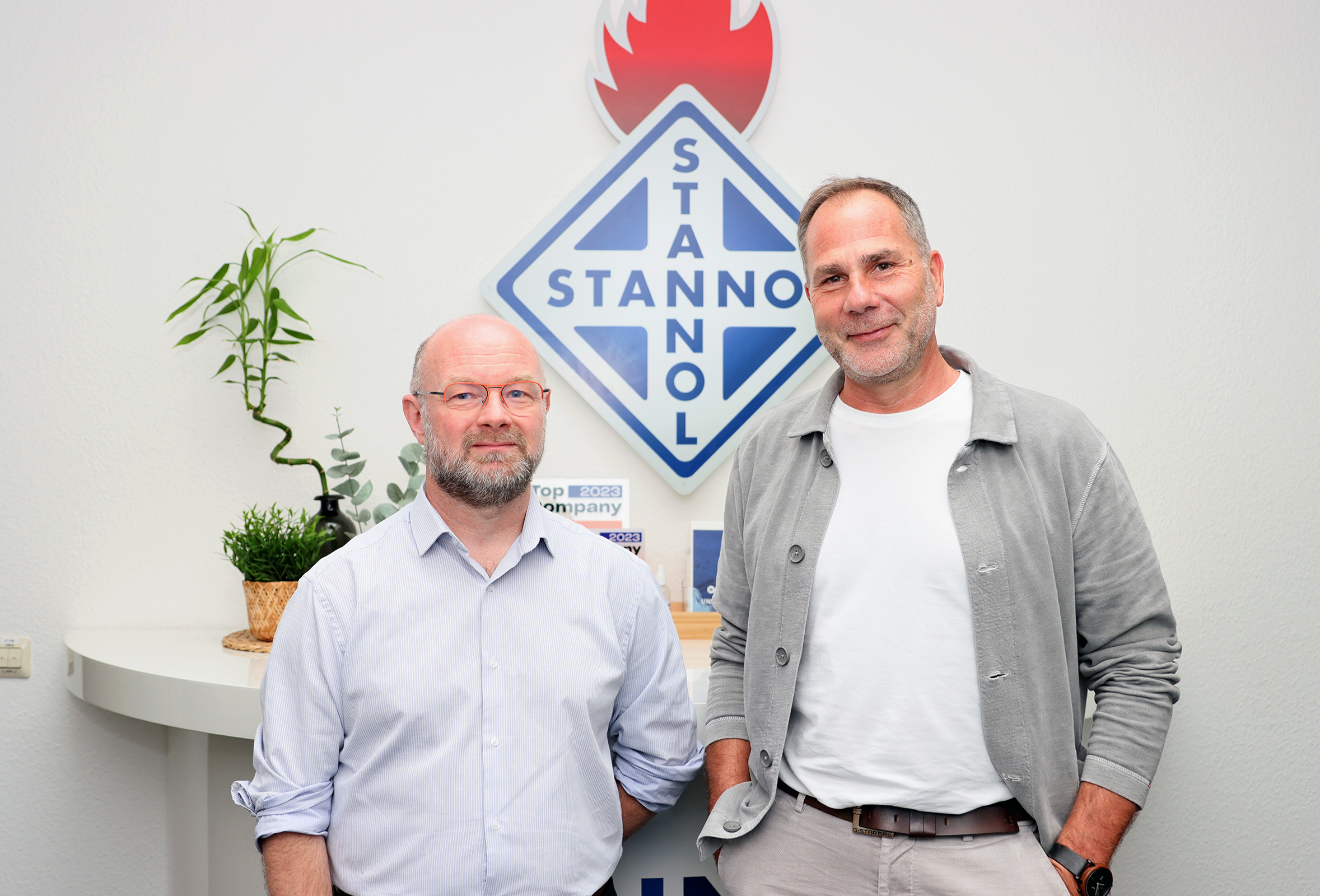 The picture shows two men in front of a large Stannol logo: Jean-Emmanuel Lechene is on the left, Thomas Kolossa is on the right. Both are smiling friendly into the camera.